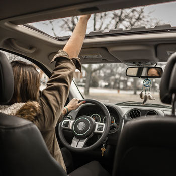 an image of a woman driving her vehicle and reaching her hand up through the sunroof