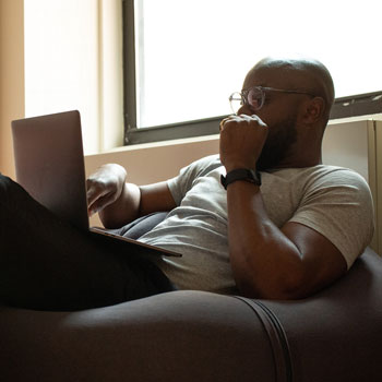 an image of a man, seating on a comfortable chair, using a laptop